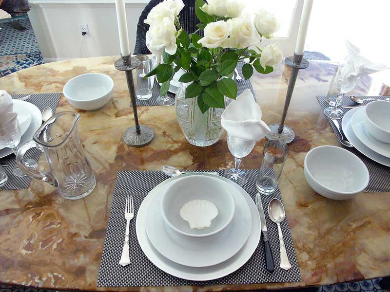 A Provençal lunch setting for four with white roses and large porcelain pasta bowls accented with decorative sea shells. Remove shells before serving!