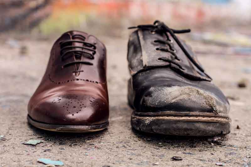 The polished shoe of a wealthy man next to the worn out shoe of a poor man.