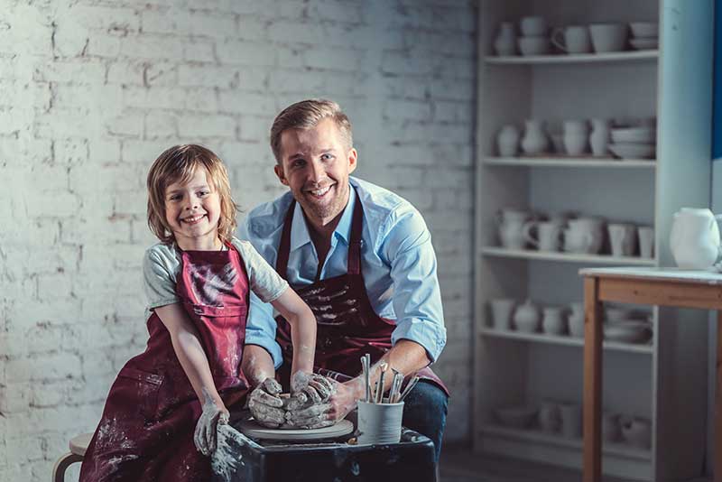 A happy father and daughter work at a pottery wheel together.